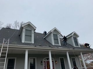 Workers on a roof with dormer windows, cloudy day.