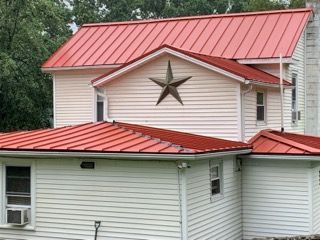 Red metal roof on a white house with a star decoration.