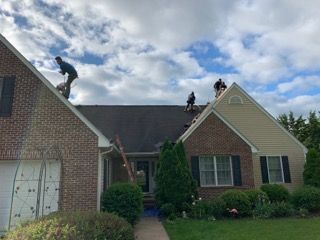 Roofers working on a house roof under a cloudy sky.