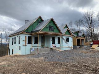New home under construction with green insulation, gray roof, and black window frames.