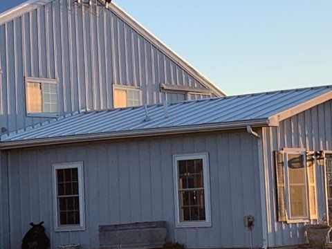 White metal-sided barn with matching roof. Windows and gutters are visible.