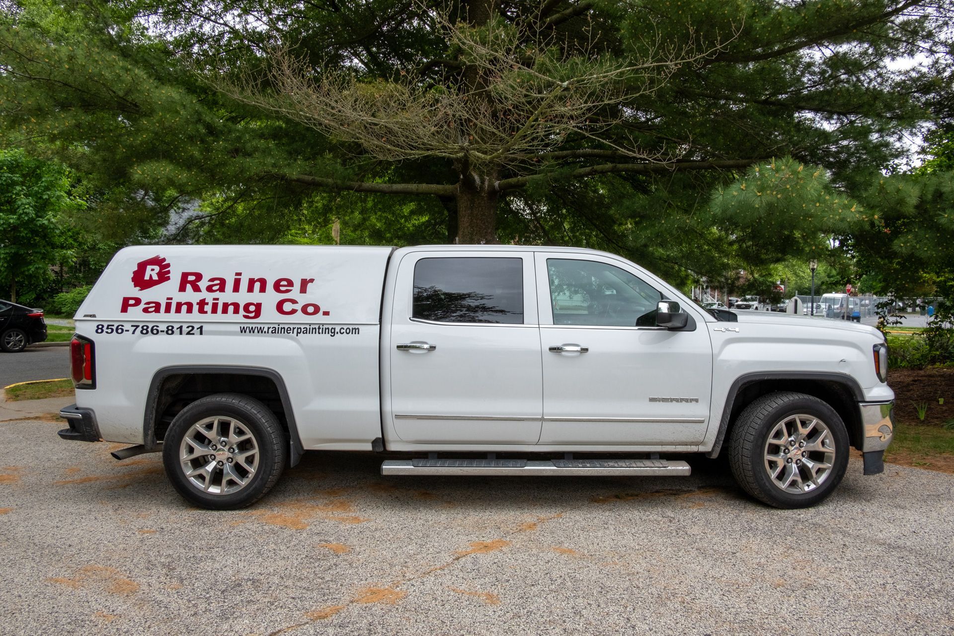 A white pickup truck with a cap is parked in a gravel lot.