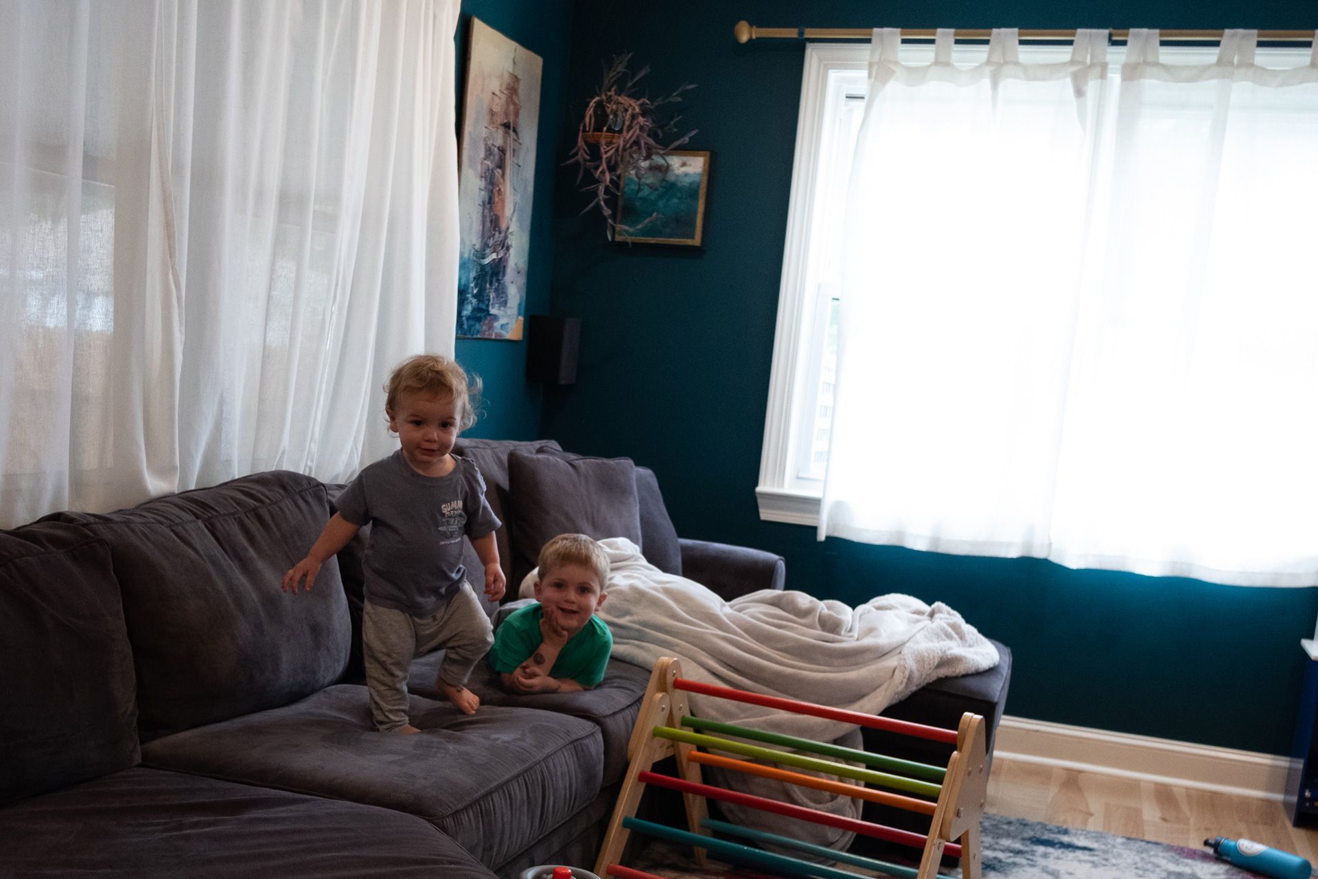 Two young boys are playing on a couch in a living room.
