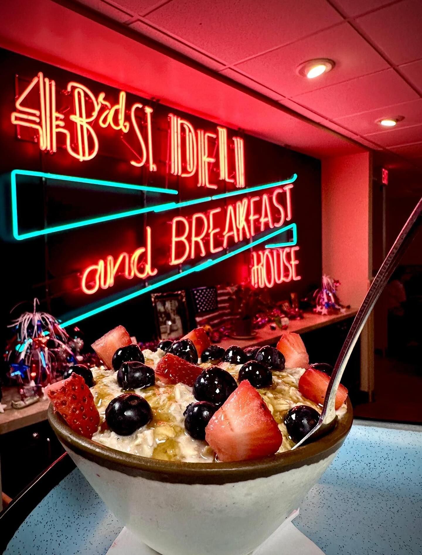 Oatmeal bowl topped with berries in a diner, neon sign in background that says “4Bs St. Deli and Breakfast House.