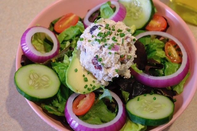 Salad with tuna salad, cucumber, red onion rings, tomatoes, and avocado in a pink bowl.
