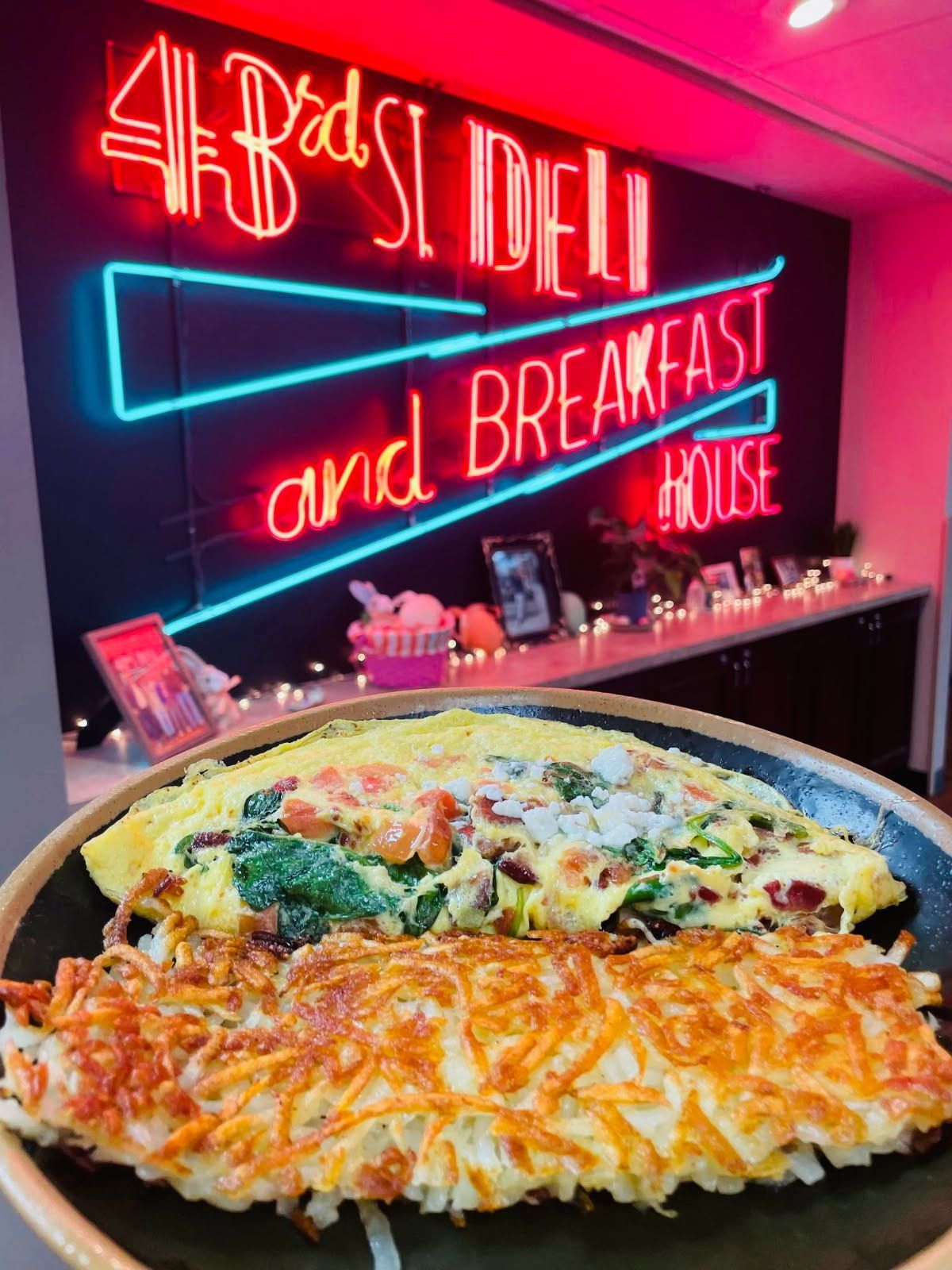 Omelet and hash browns on a plate in front of a neon sign for a deli/breakfast house.