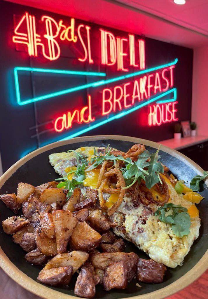 Omelet and potatoes on plate; neon sign for deli/breakfast house in background.