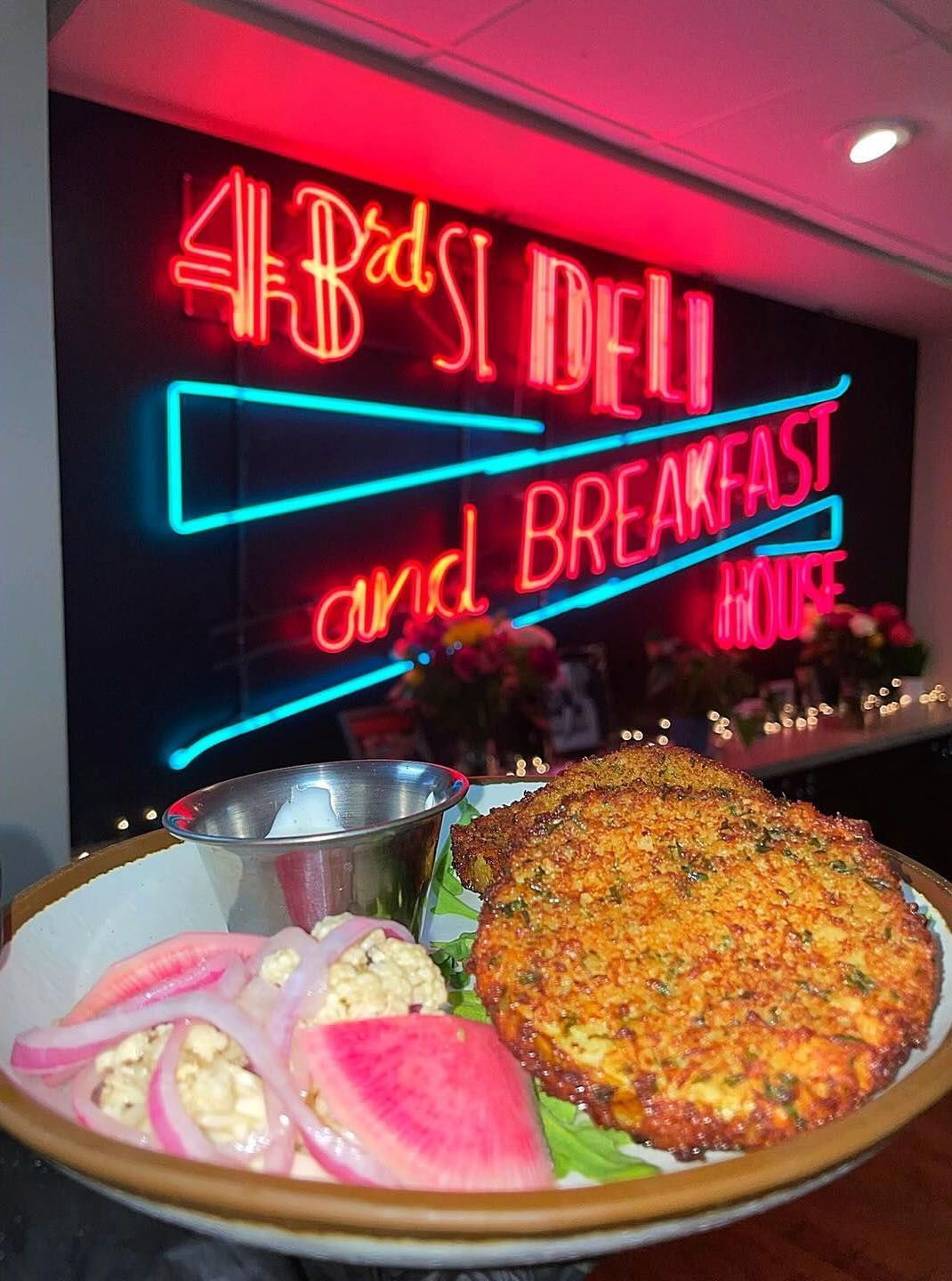 Plate with fried food, onions, and sauce in front of a neon sign that says
