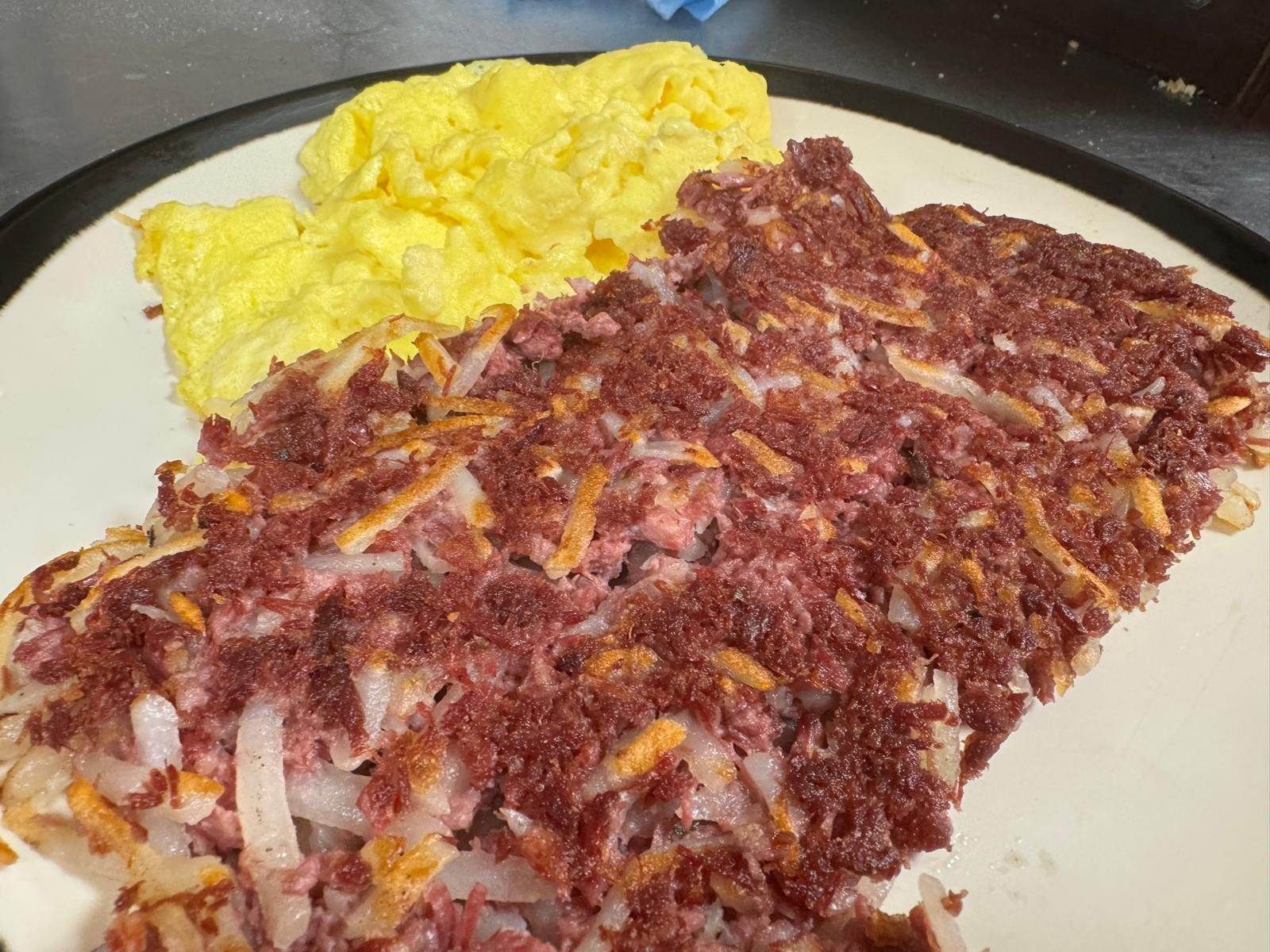 Scrambled eggs and corned beef hash on a white plate.