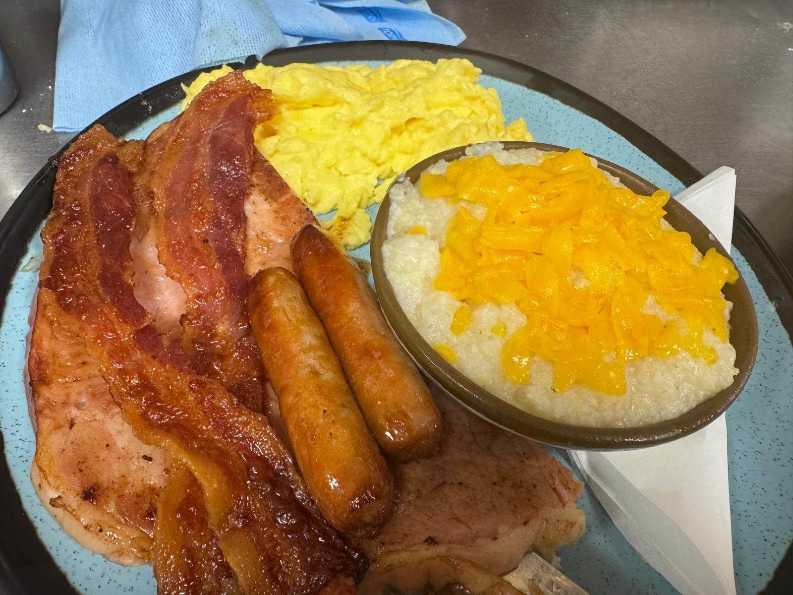 Breakfast plate with bacon, sausage, scrambled eggs, cheese grits.
