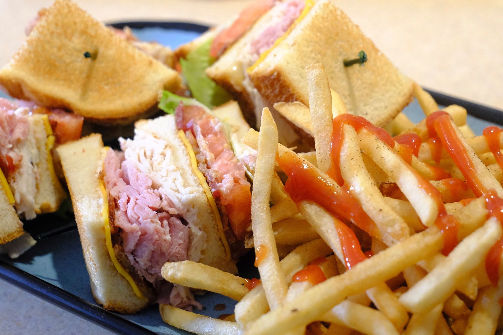 Club sandwich with fries, topped with ketchup, on a blue plate.
