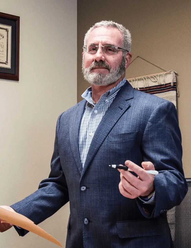 Man in blue blazer speaking at a podium, holding a pen in an office setting