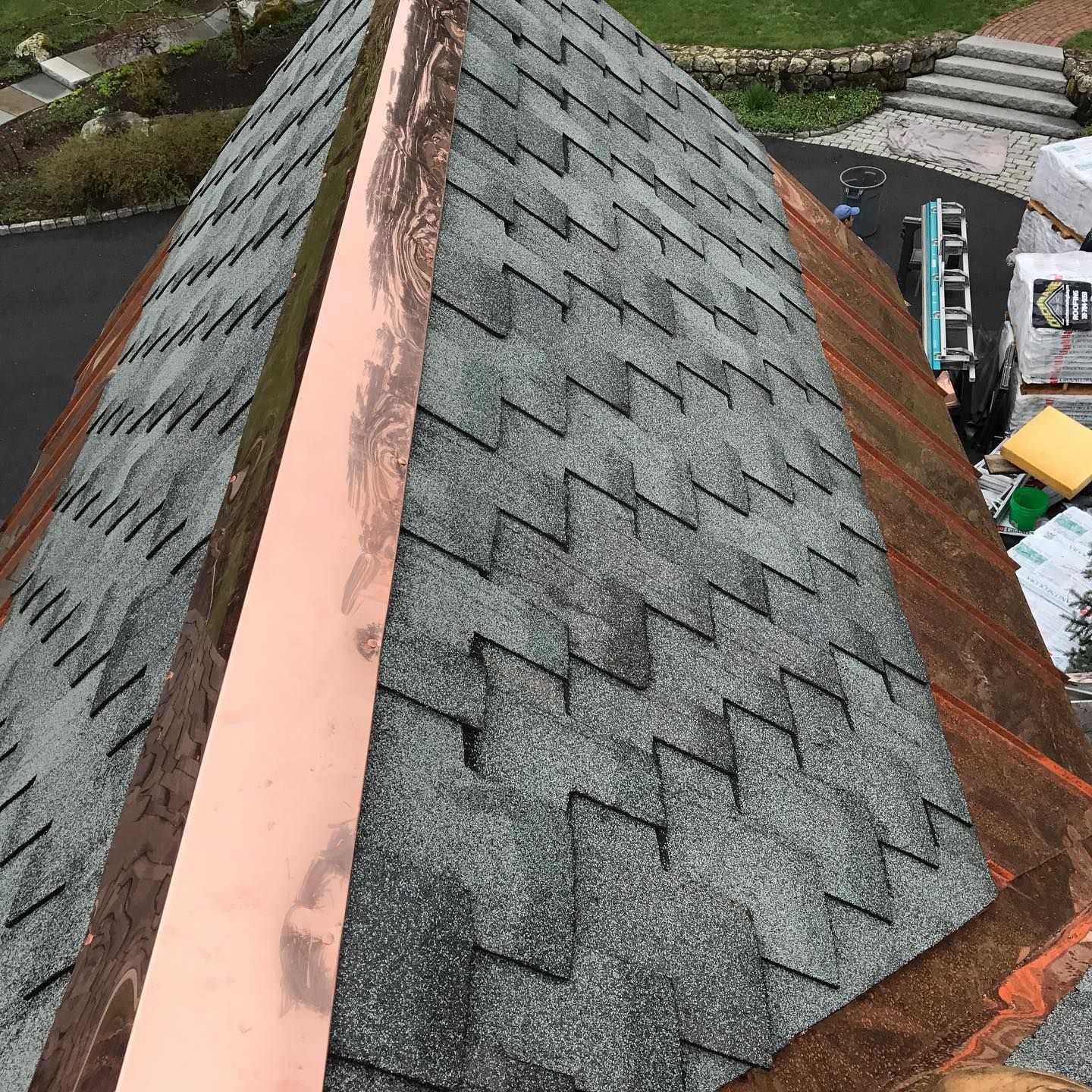 View of a dark shingled roof with copper flashing along the peak; supplies in the background.