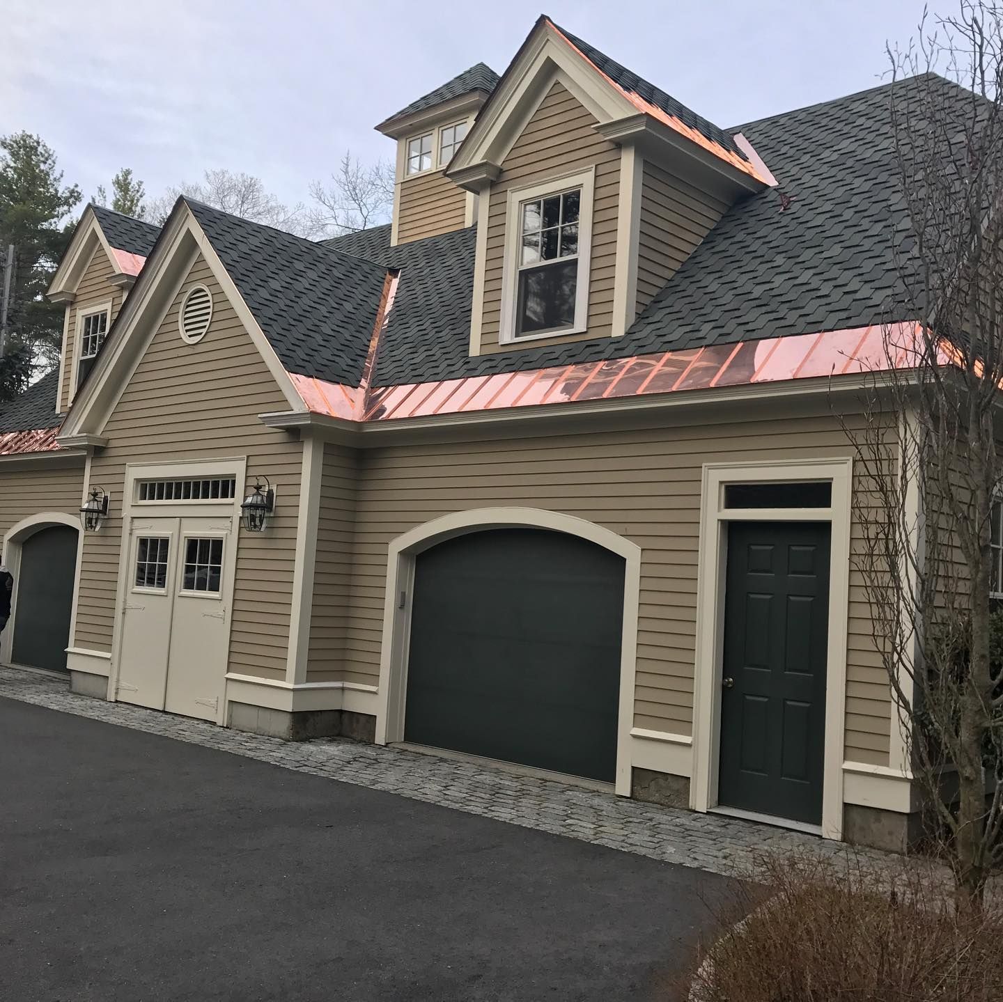 Tan and copper garage with black roof and three garage doors, nestled in front of trees.
