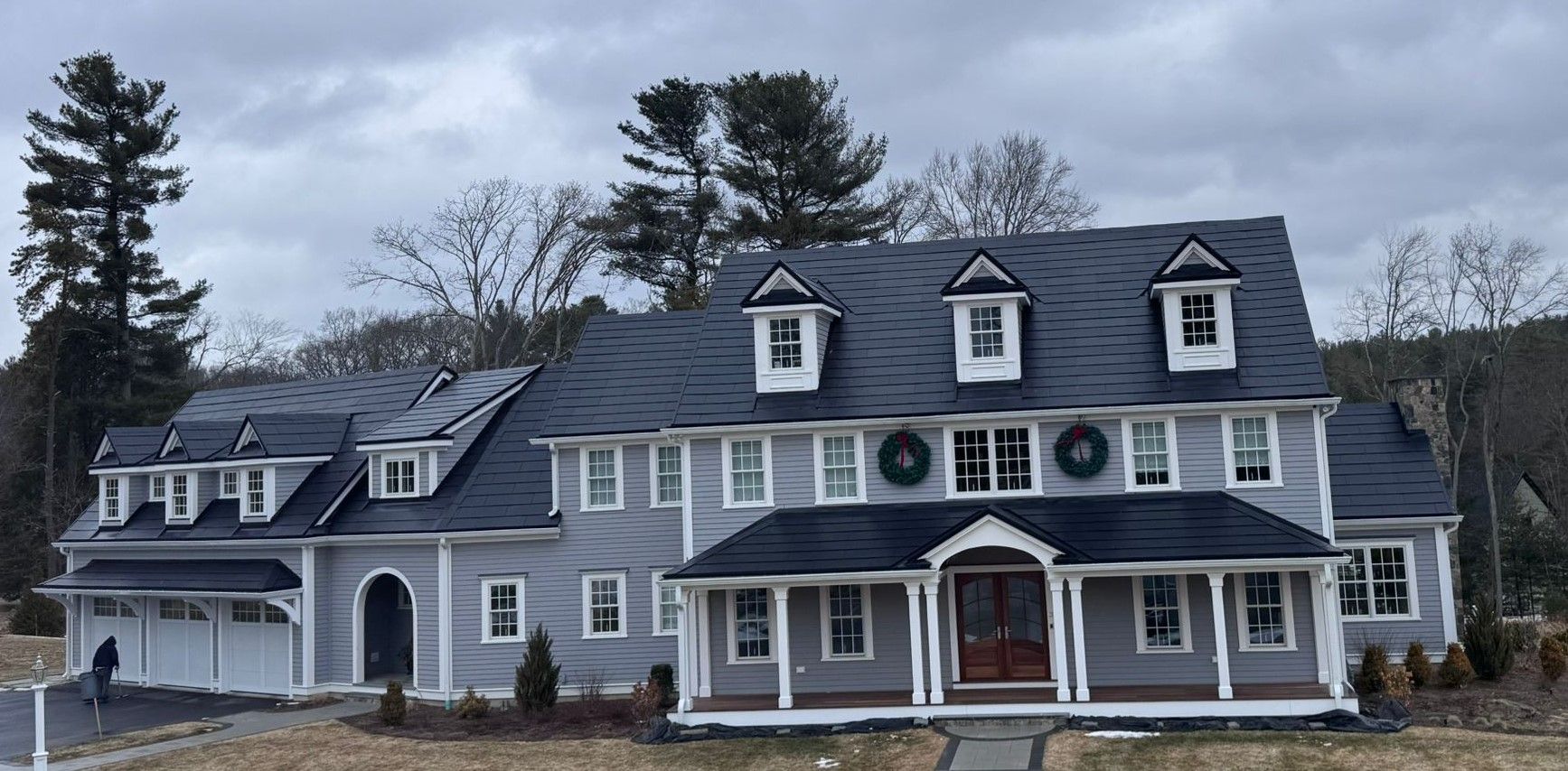 Large gray house with black roof, many windows, and a porch. Cloudy sky.