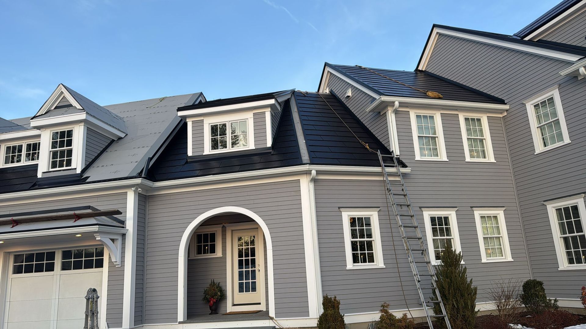 Gray and black residential building with a ladder leaning against it on a sunny day.