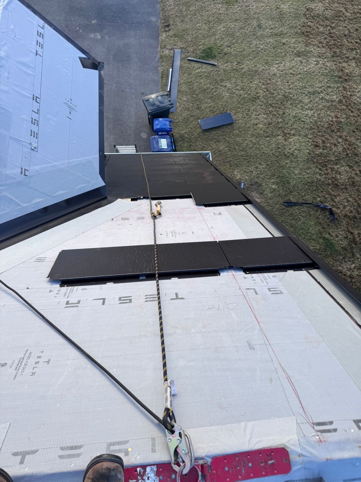 Roofer on a roof wearing safety harness, replacing shingles. Safety rope attached.