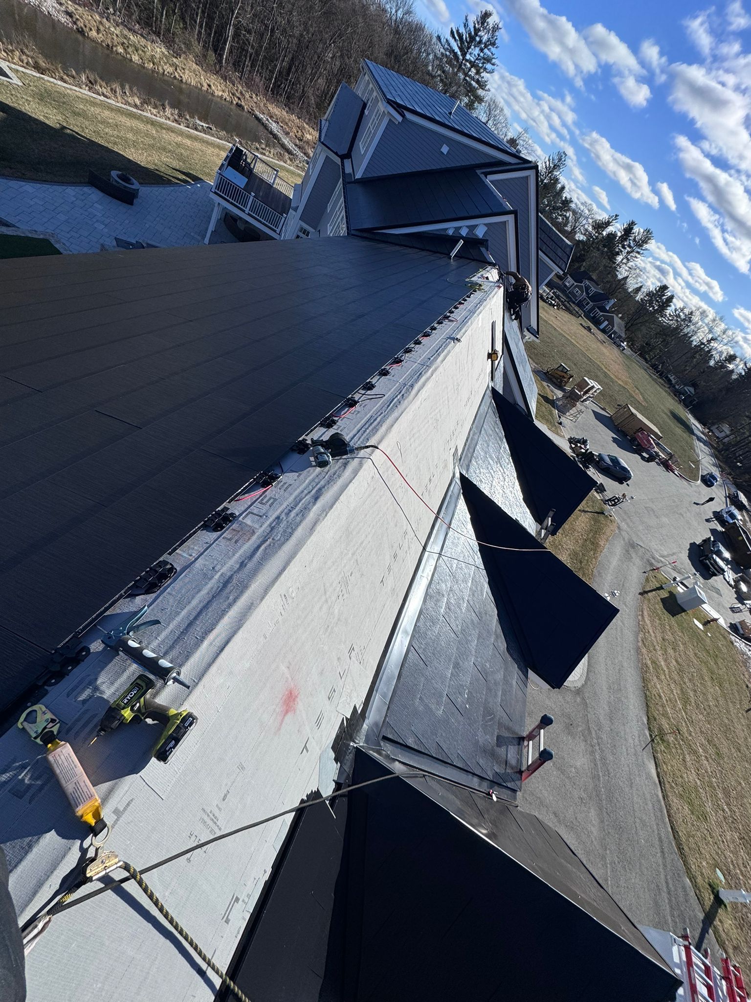 Black rooftop with solar panels, a long grey section, and a blue sky with clouds.