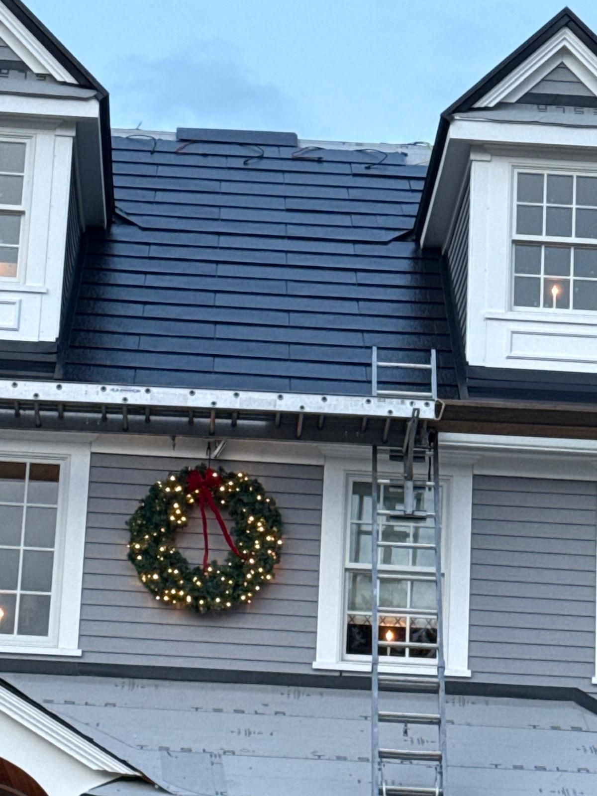 A house with a slate roof, Christmas wreath, and a ladder against it.