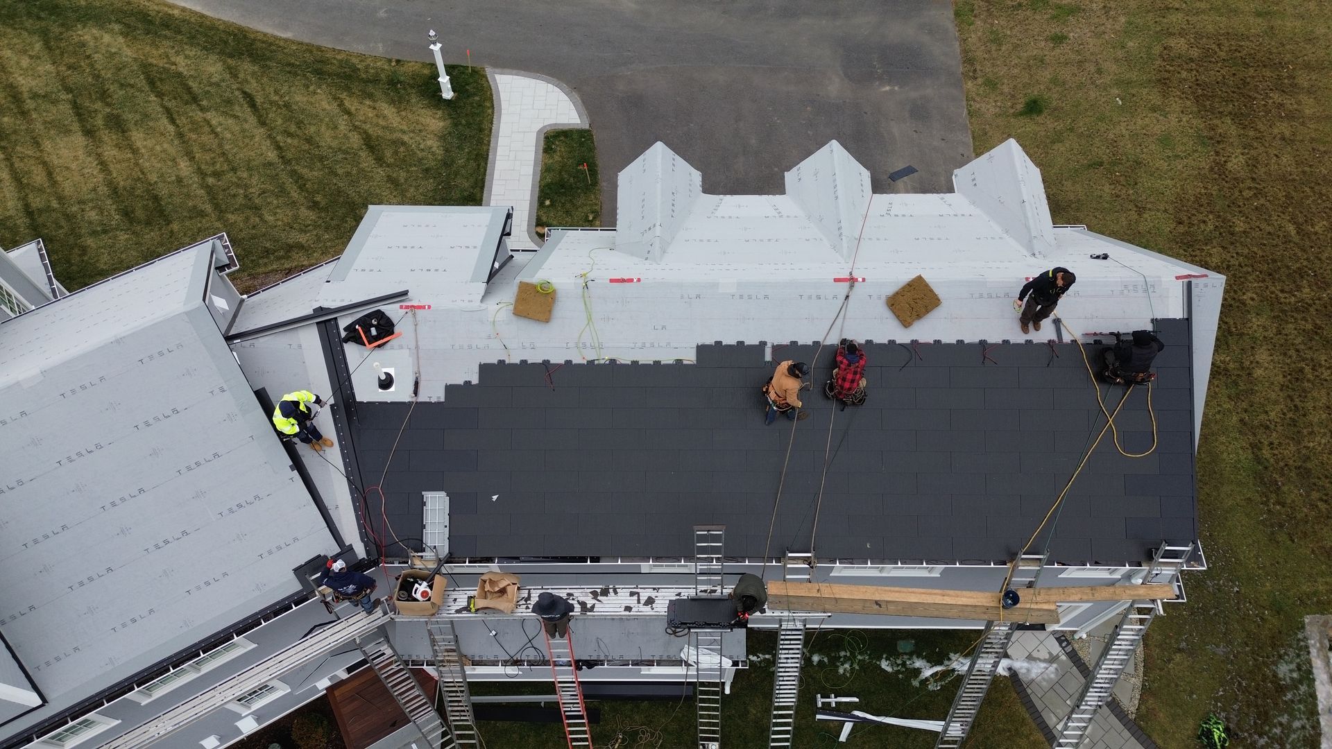 Workers installing dark roofing on a building; some on scaffolding.