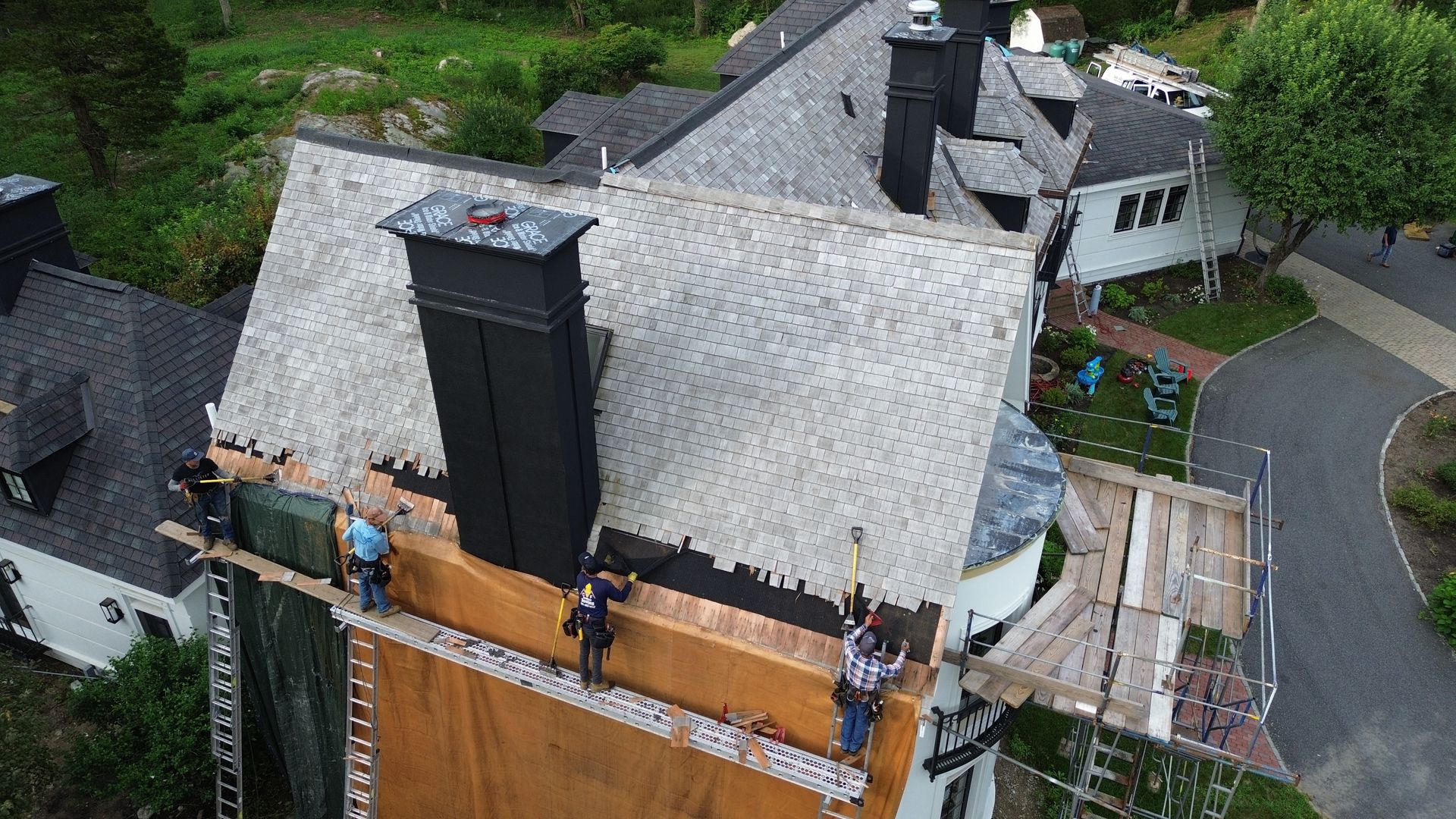 Workers on scaffolding, installing copper on a roof near a chimney.
