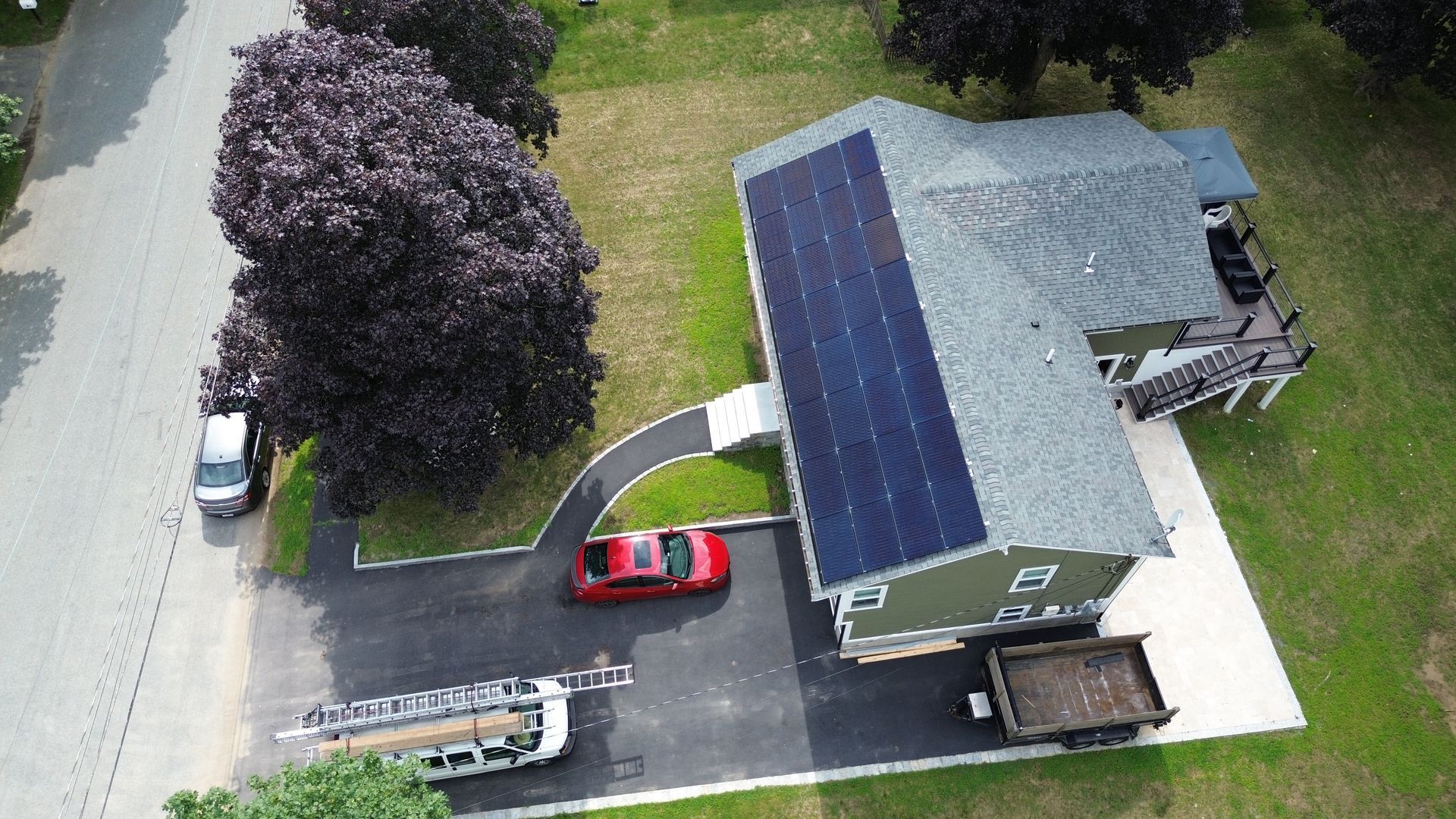An aerial view of a house with solar panels on the roof and vehicles parked in the driveway.