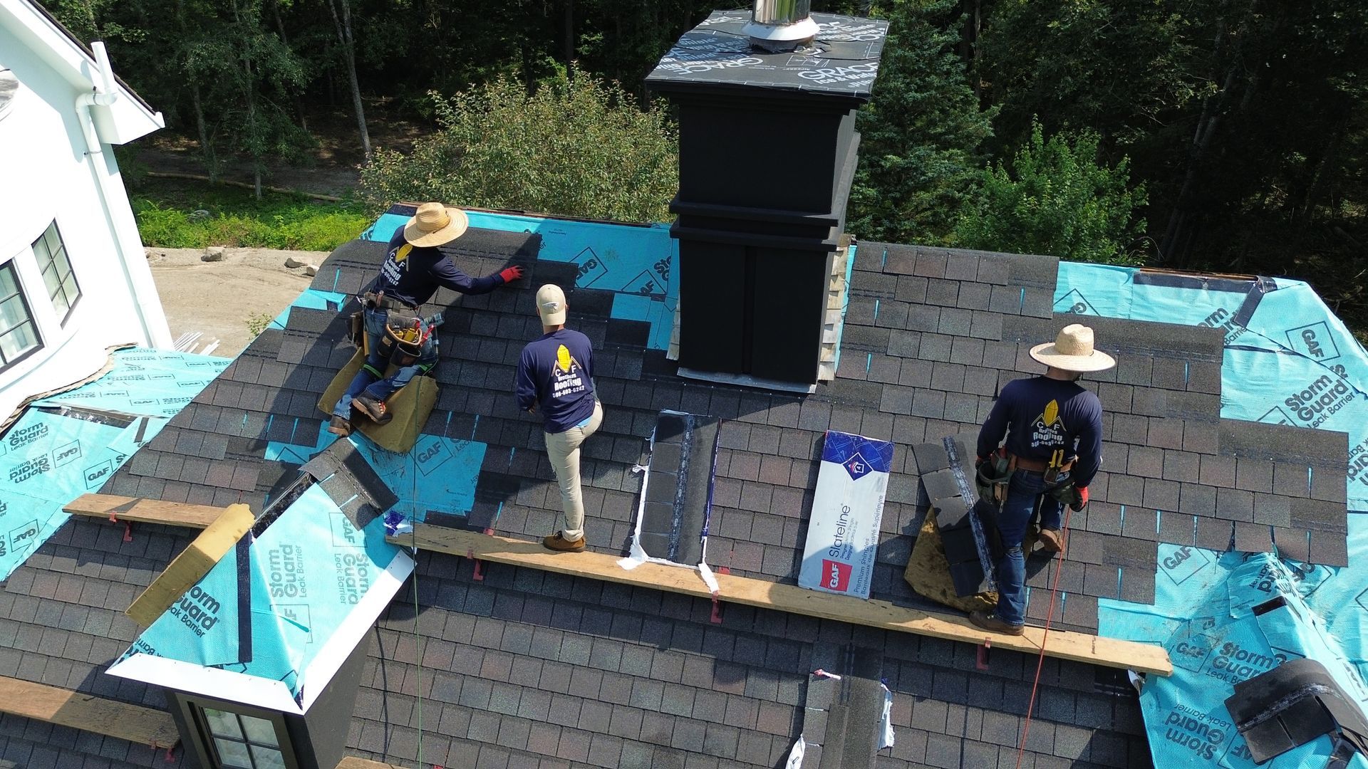Roofers installing shingles on a house roof near a chimney.