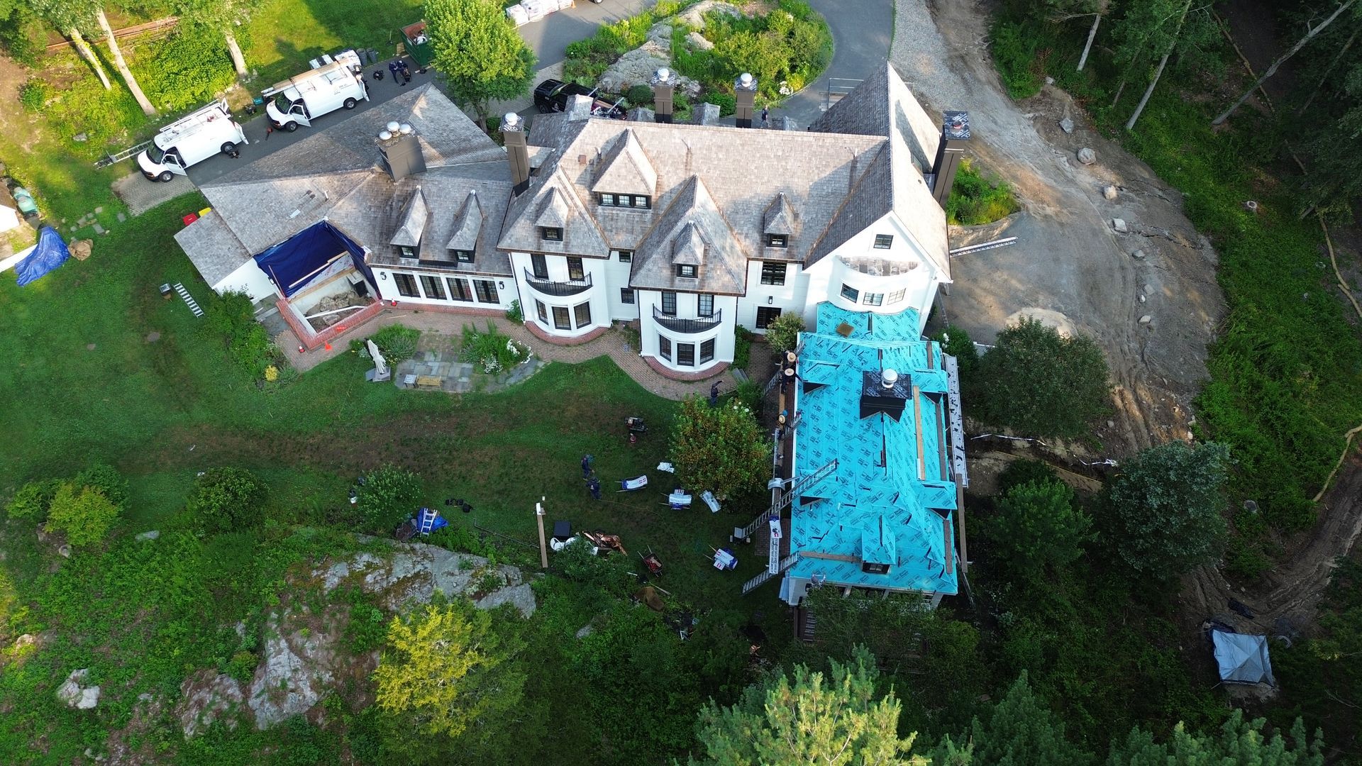Aerial view of large house under construction with blue tarp on the roof.