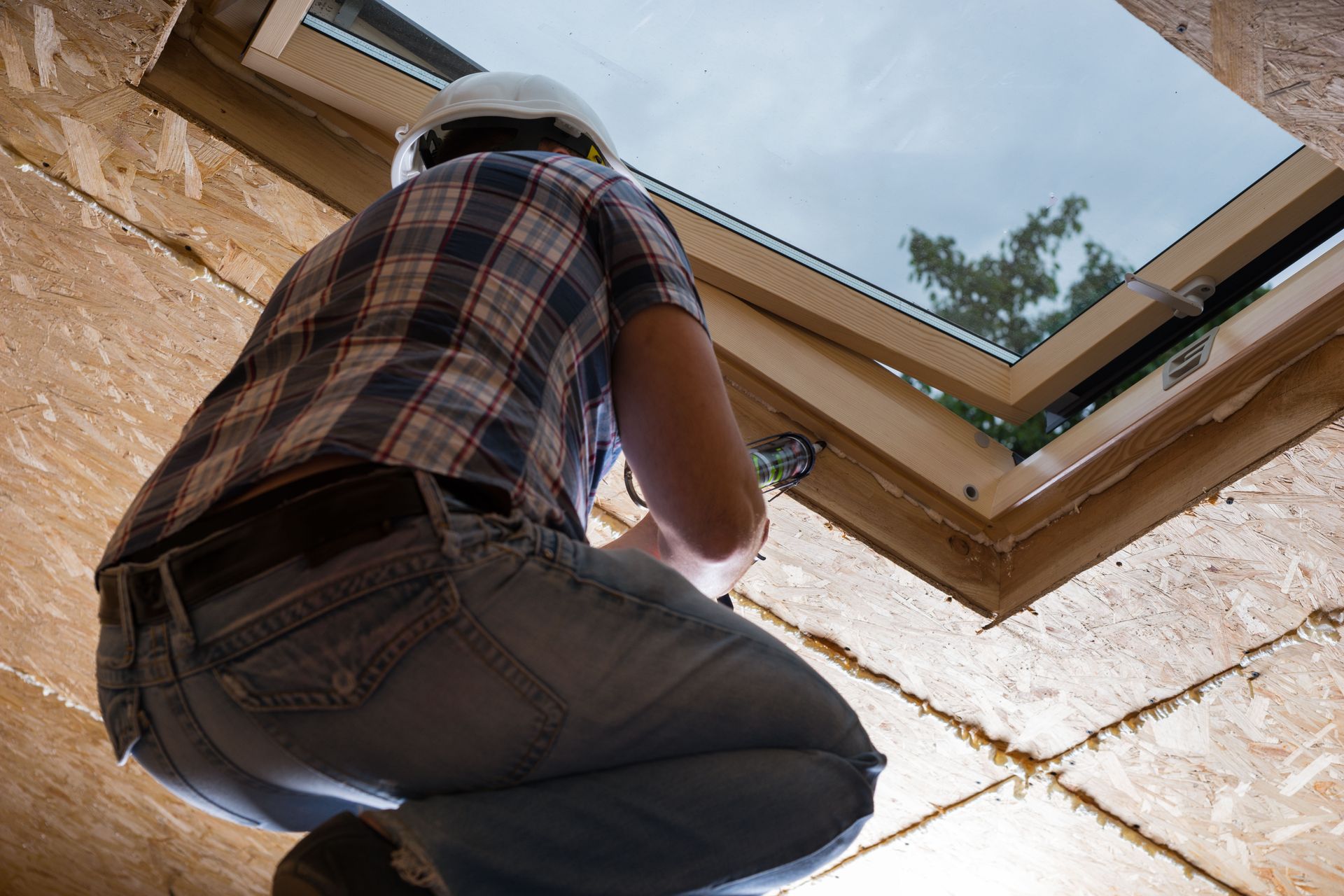 Person installing siding on a building, wearing a tool belt and gloves.