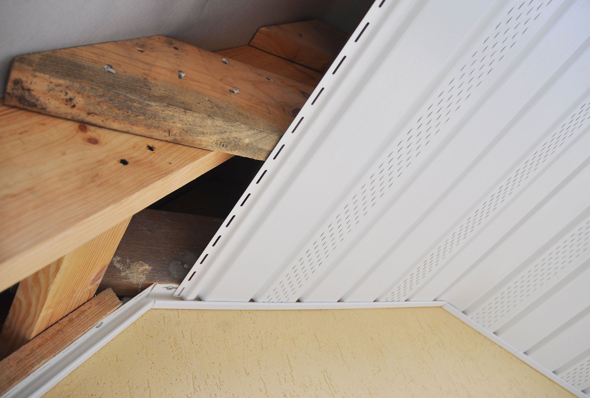 White vinyl soffit installed on wooden rafters, against a tan wall.