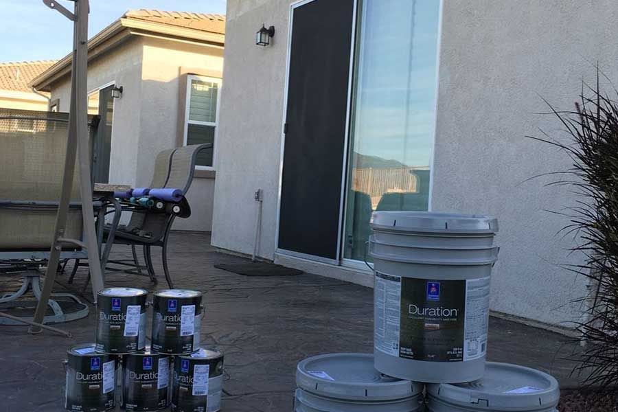 Paint cans stacked on a patio. A house with a sliding glass door is in the background.