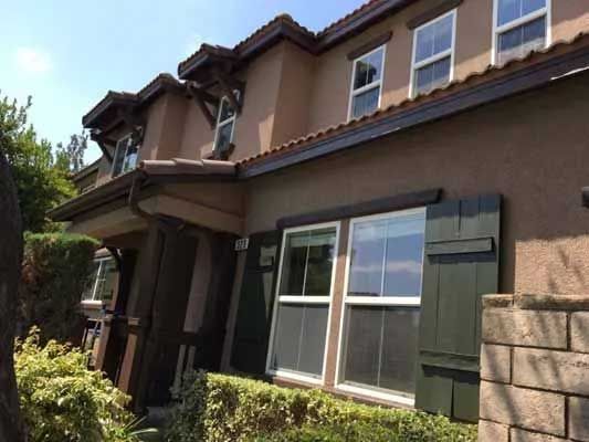 Two-story brown stucco house with green shutters, windows, and brown roof.