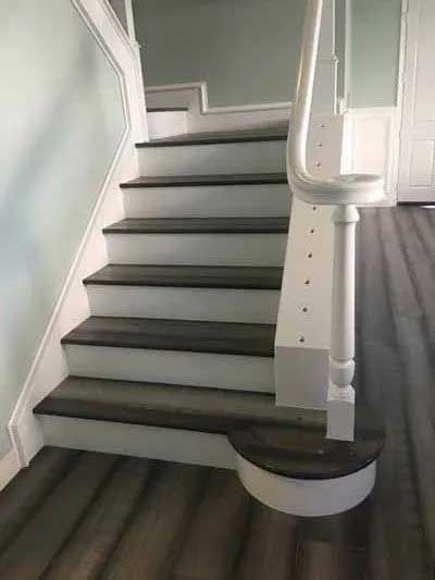 Staircase with white trim, gray treads, and a curved bottom step. Interior view with light blue walls.