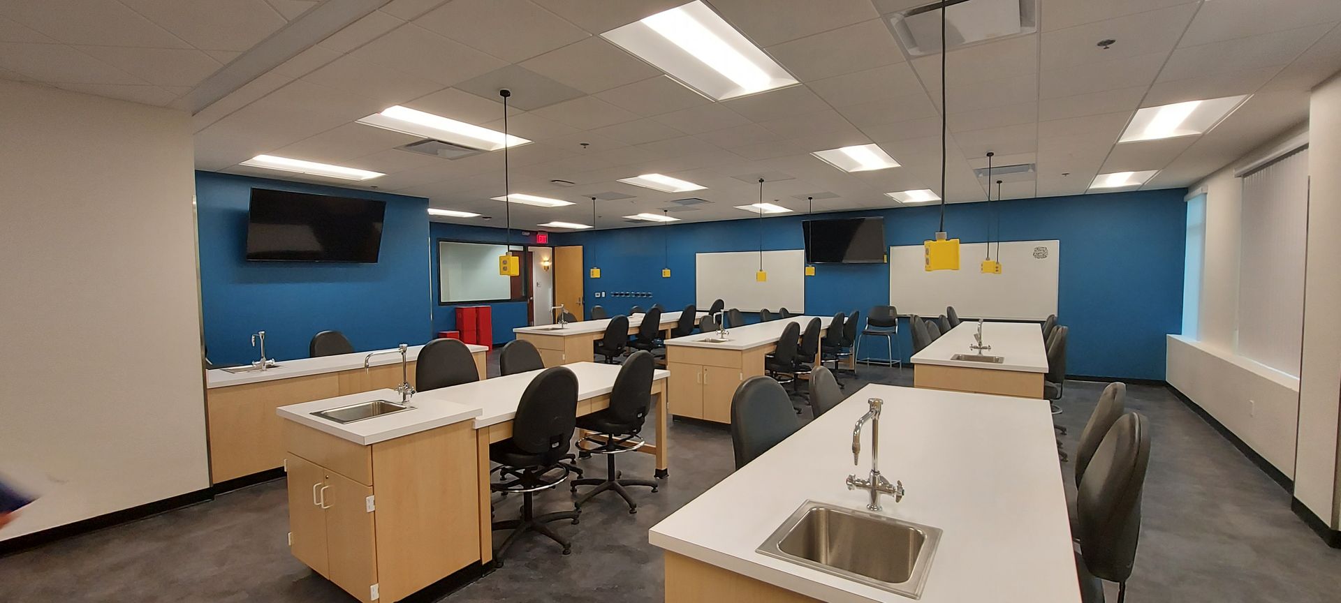 A large classroom with lots of tables and chairs and a sink.