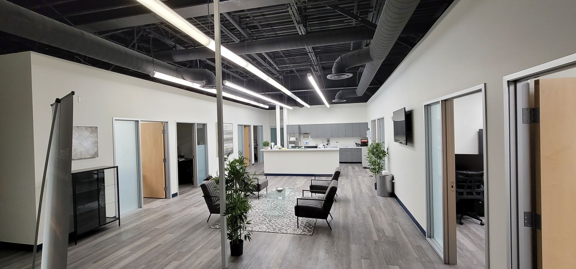 A long hallway in an office building with a lot of doors and chairs.
