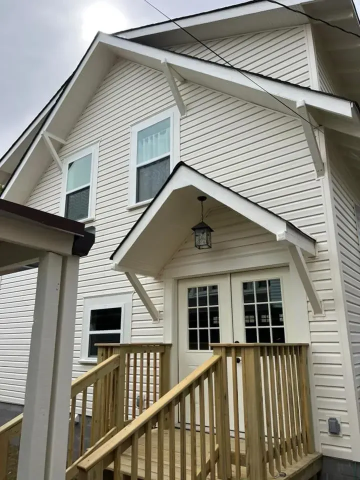 A white house with a wooden deck and stairs leading to it.