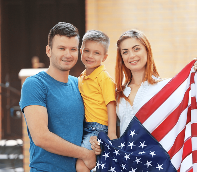 Family holding an American flag, smiling indoors.