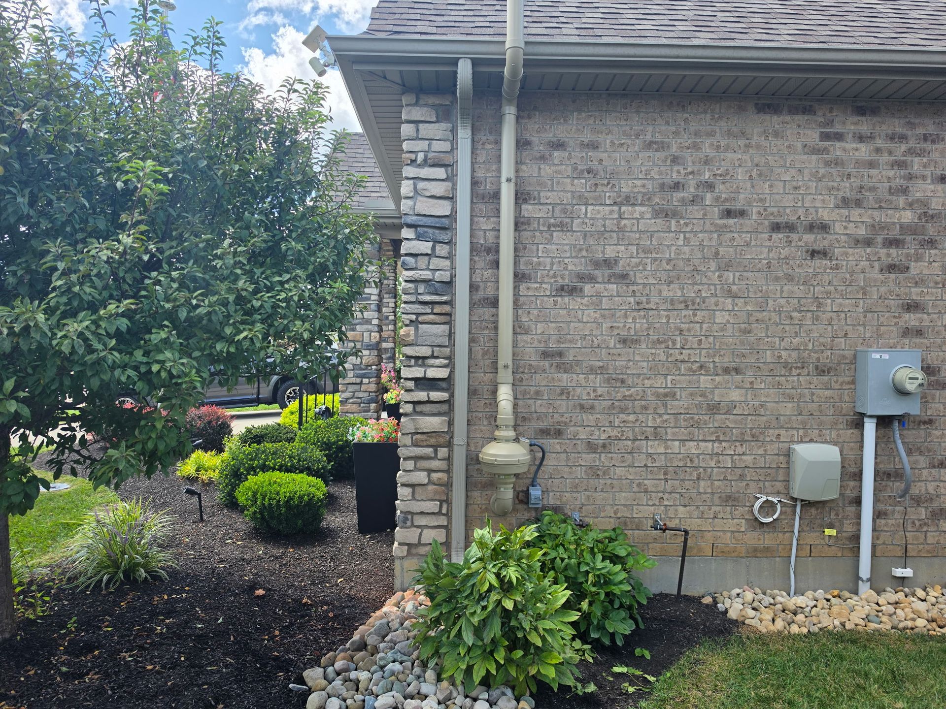 Brick house side yard with shrubs, mulch beds, downspout, and utility meters