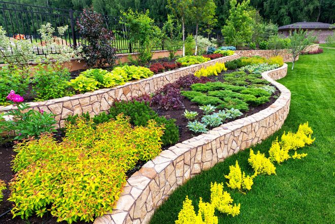 Curved stone garden bed with colorful flowering plants and lush greenery in a landscaped park