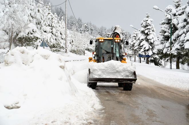 Snowplow clearing a snowy road beside snowbanks and trees in winter