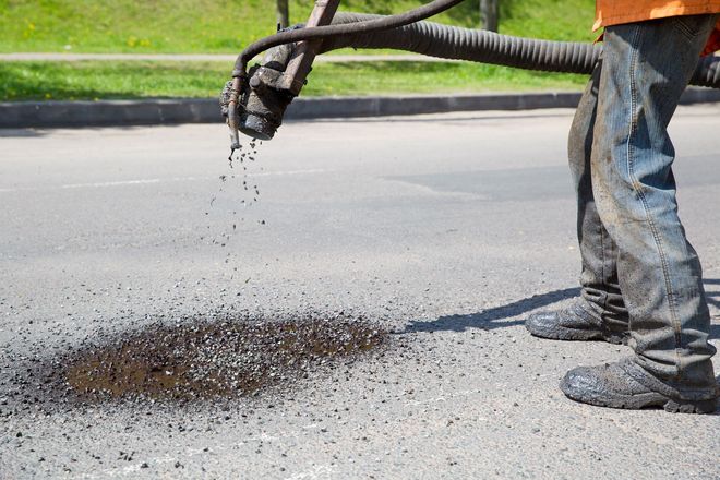 Worker spraying asphalt patch on road from a hose attached to a truck
