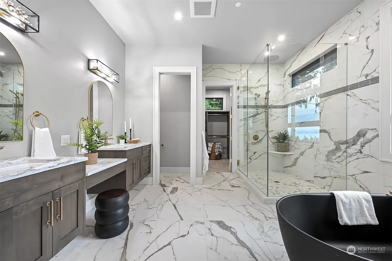 A bathroom with a black tub , two sinks , and a walk in shower.