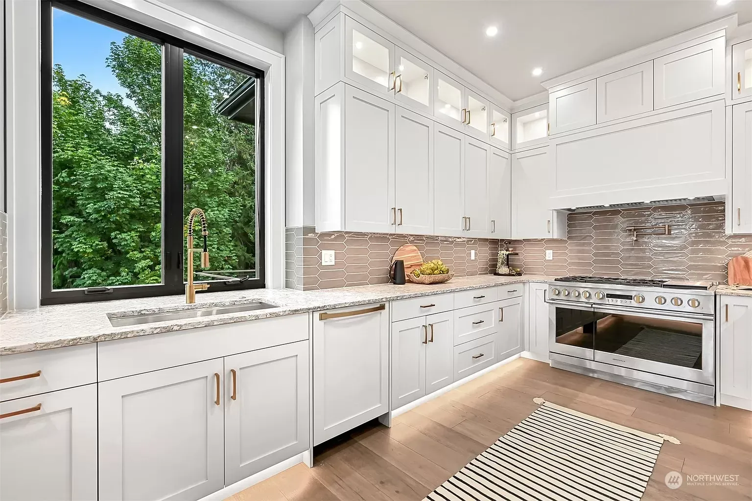 A kitchen with white cabinets , granite countertops , stainless-steel appliances and a large window.