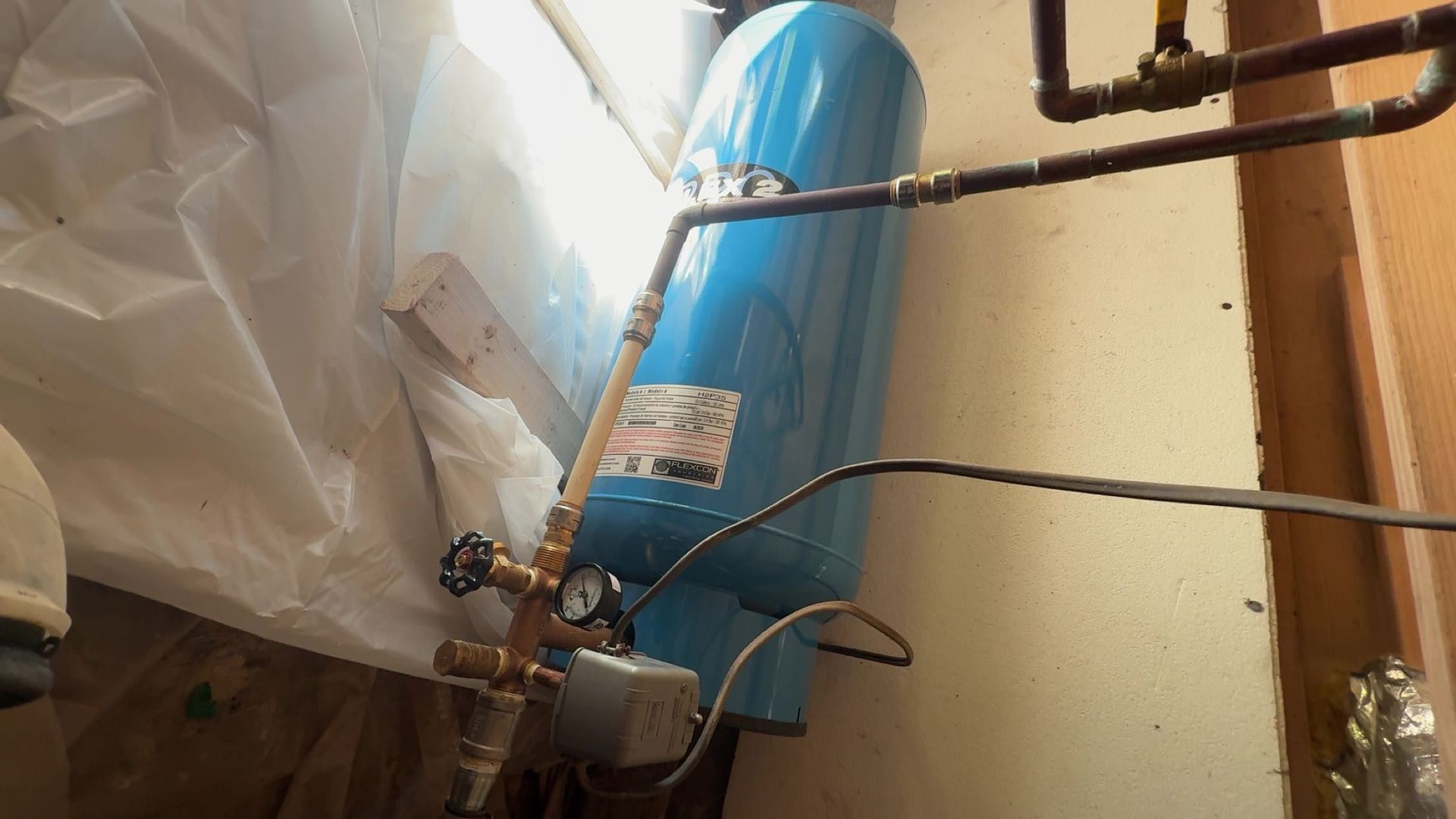 Blue water heater with pipes and wires in a cramped utility closet