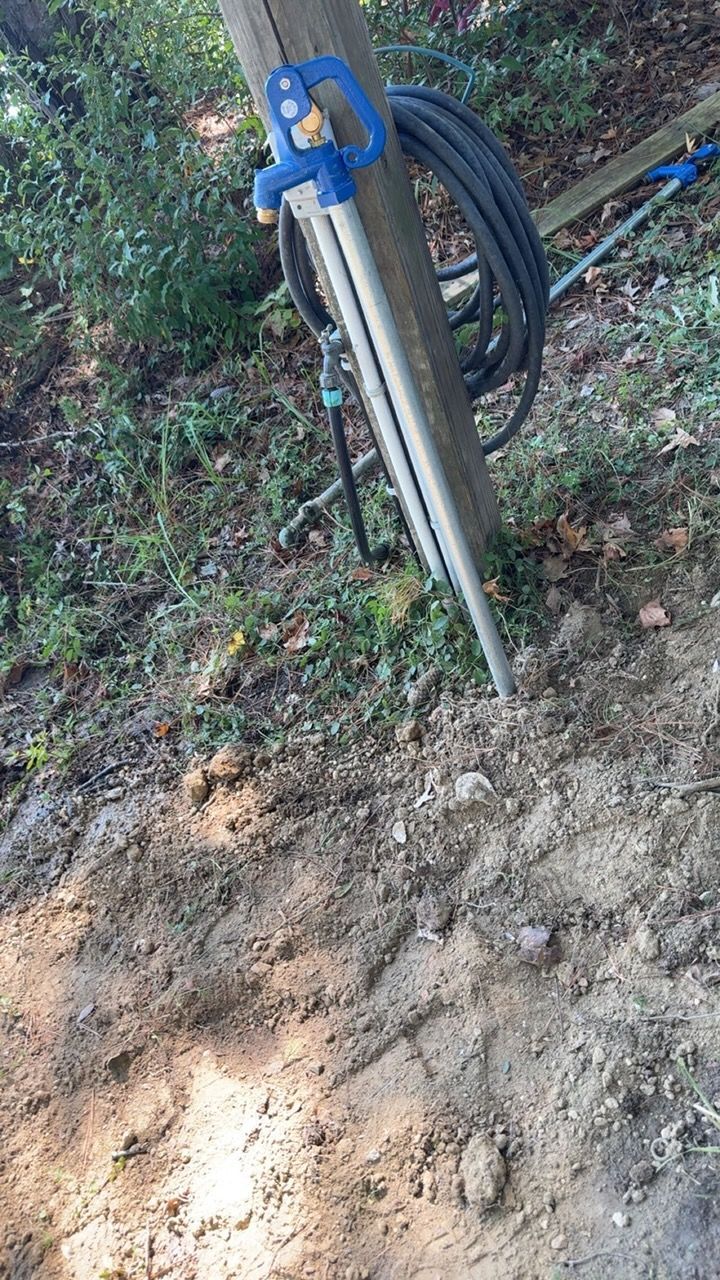 Blue utility hose reel mounted on a metal post beside a dirt path in a wooded area