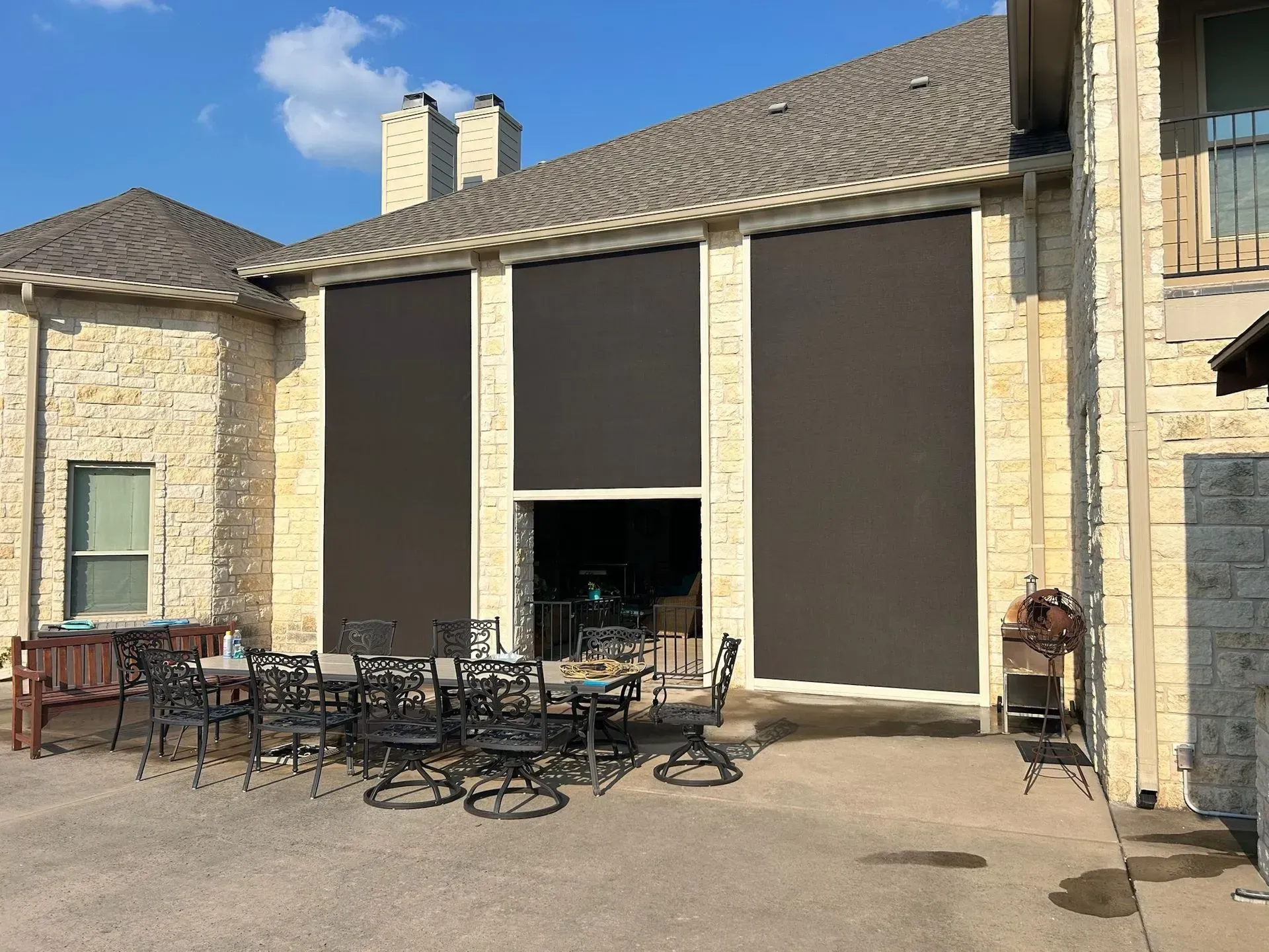 Patio with retractable awning, outdoor kitchen, stone wall, and clear blue sky.