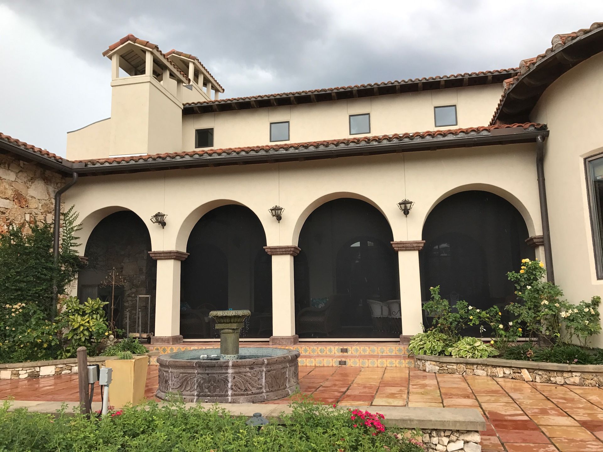 Beige stucco house with arched doorways, black screens, and a fountain in a courtyard.