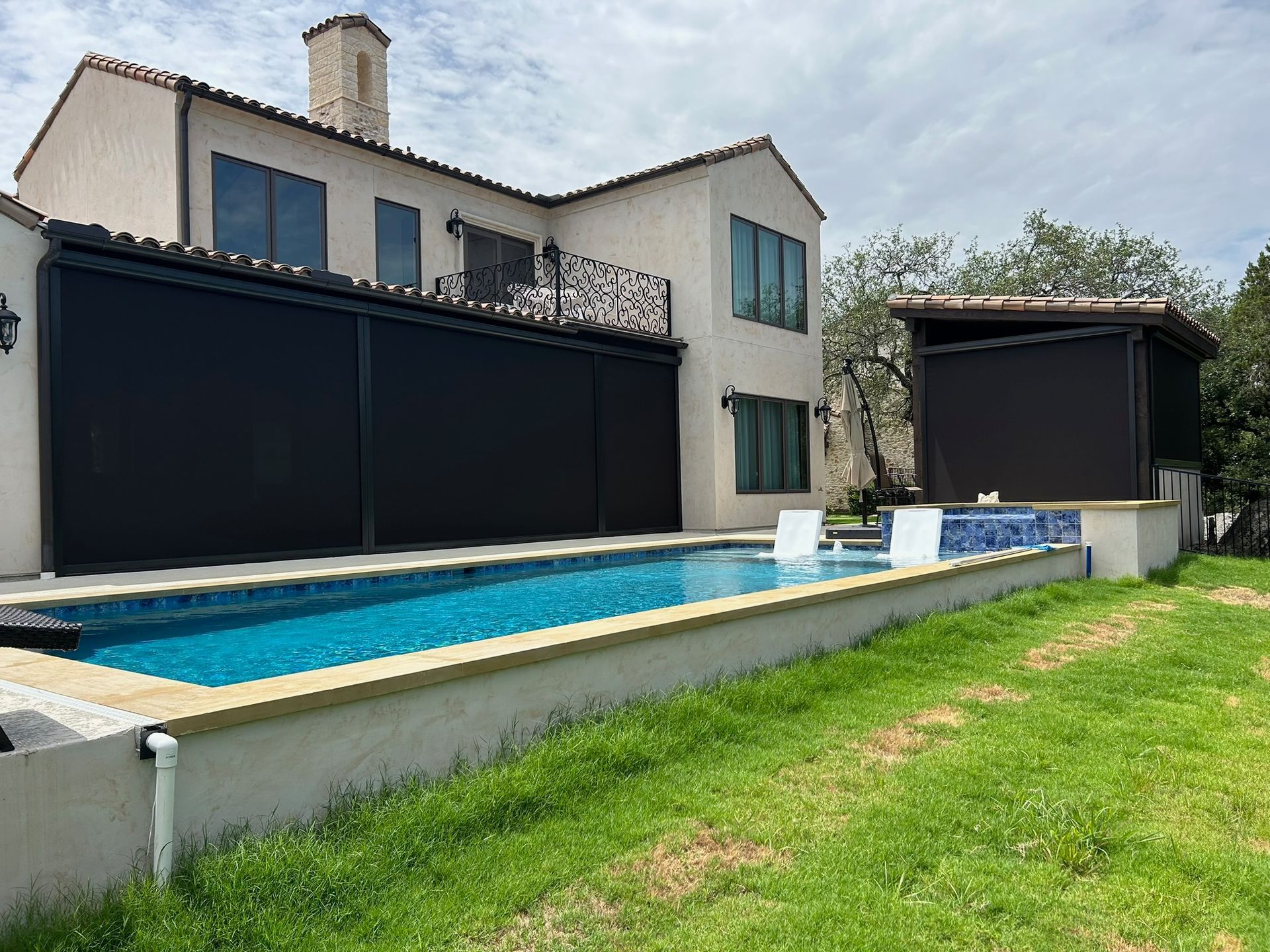 Pool with black screens on a house, small pool house, and green lawn.