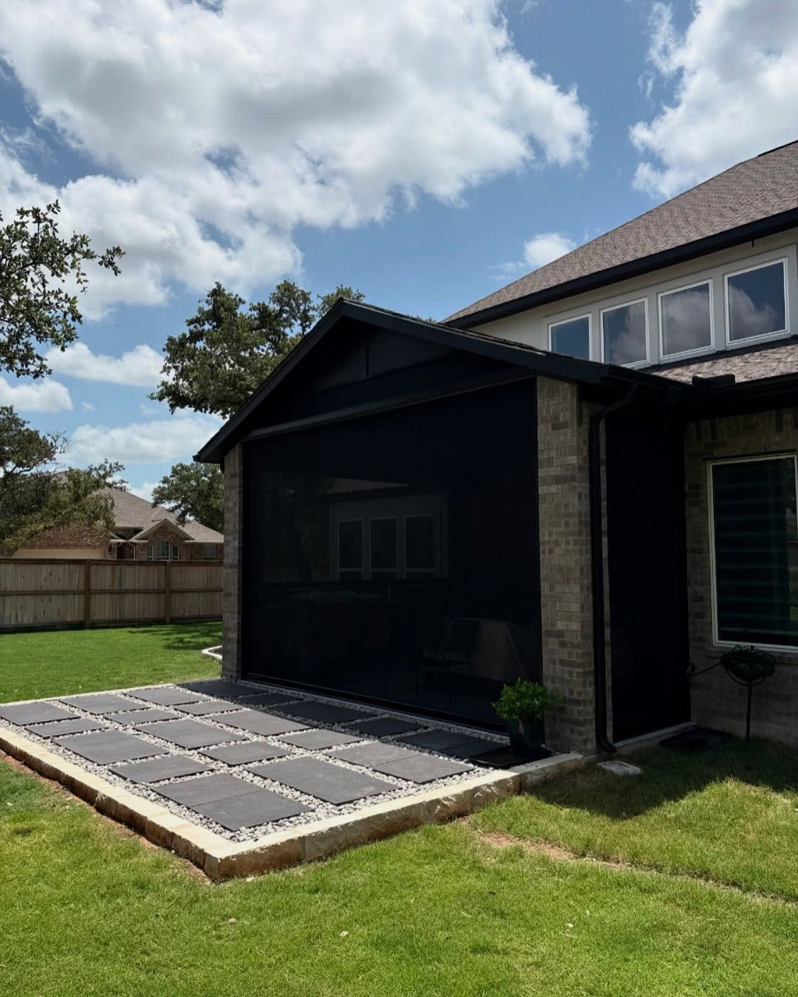 Black screened-in patio attached to a two-story brick house with a stone patio and green lawn.