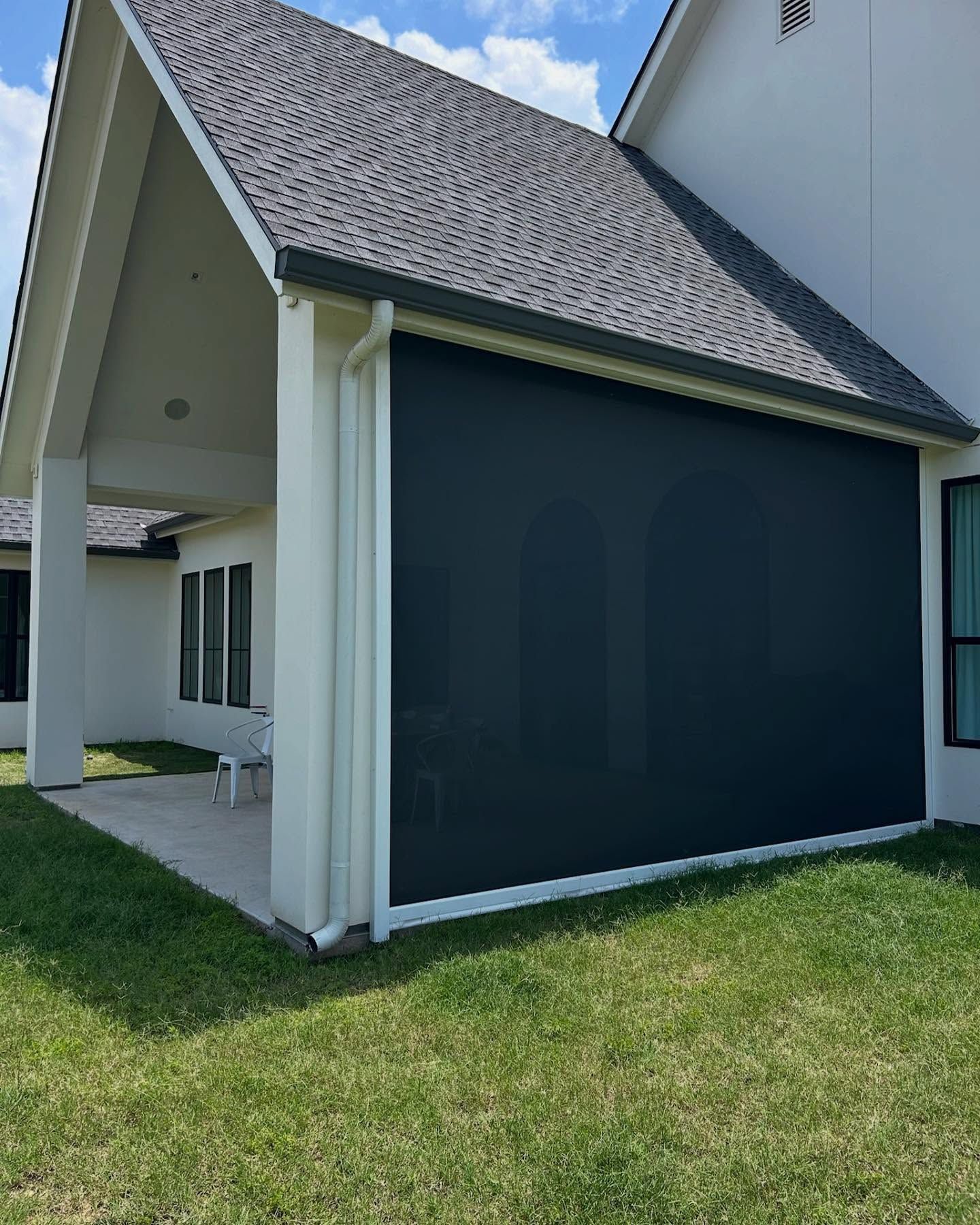 Black outdoor screen on a house's covered patio. Beige columns, white trim, grey roof. Green grass in the foreground.